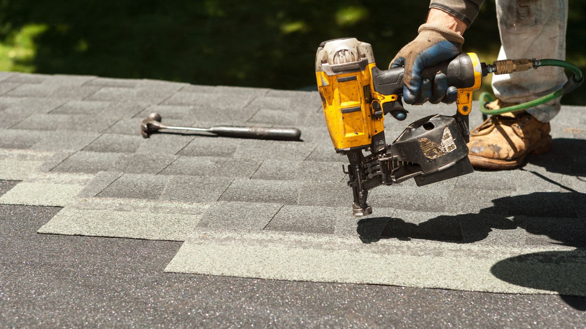 Roofer using a nail gun to install asphalt shingles